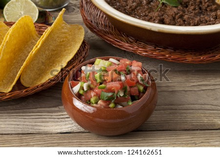 Bowl of pico de gallo, near a plate of ground beef and tacos