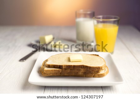 Glass of milk, juice, butter and bread slices on a white table