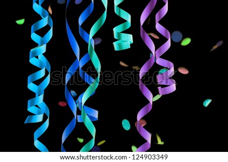 Detail of curling party ribbons and falling confetti isolated on black background