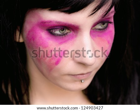 A woman with pink make up smeared on her face looks away from the camera.