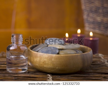 Close-up image of spa massage stones with a bottle of essential oil and lighted candle