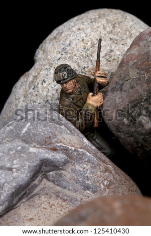 Close-up image of a toy soldier miniature holding a gun and hiding on the rocks
