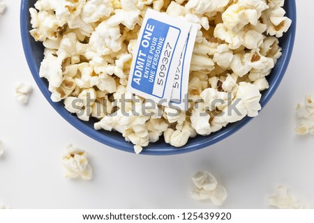 Cropped image of a popcorn bowl with movie tickets placed in a white background with popcorn spills