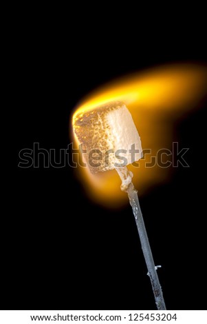 Close-up image of a stick with a burning marshmallow on fire over the dark background