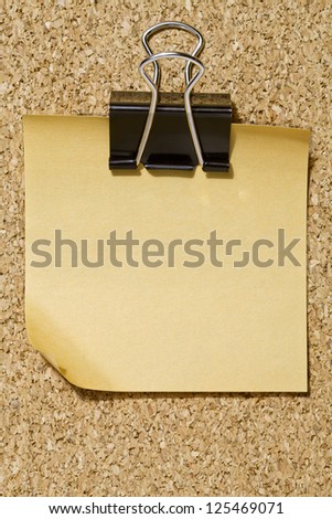 Yellow memo note with black binder clip over a cork board background