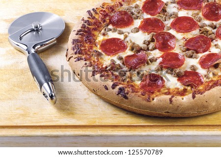 Close-up cropped shot of pizza cutter and pizza on wooden board.