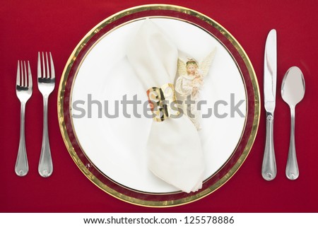 Silverware and plate with white napkin and angel decoration on a red background