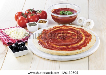 Tomato paste spread on raw pizza dough with grated cheese, black olives, tomato sauce and tomato