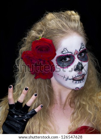 Close-up portrait of a scary woman wearing traditional sugar skull make-up against dark background.