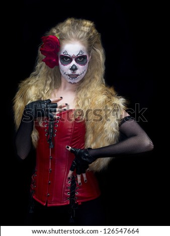 Portrait shot of a woman wearing traditional sugar skull make-up and posing over plain black background.
