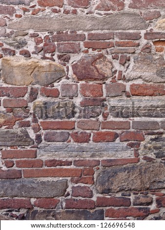 Clean image of old world wall with red bricks, raw stone and various block of different shapes and sizes.