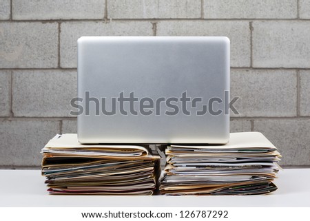 Image of a laptop kept on pile of folders against brick wall.