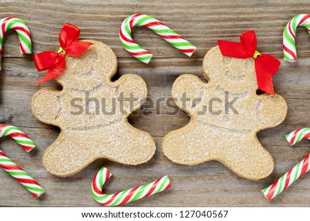 Close-up detailed shot of female gingerbread cookies with candy canes on a wood surface.