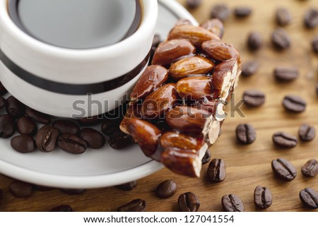 Close-up cropped shot of black coffee cup with almond confection and coffee beans.