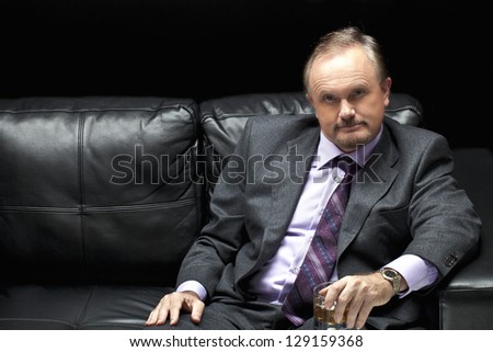 A horizontal image of a man wearing formal suit sitting on a black leather sofa