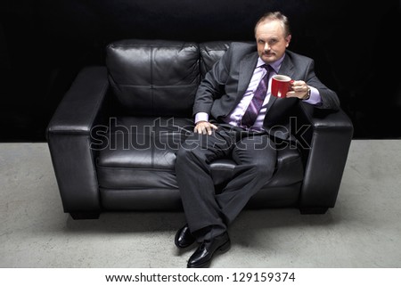 Portrait shot of a gangster in full suit sitting on couch with coffee cup