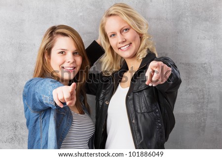 We want you - young smiling girls pointing with the finger at the camera. Studio shot against a gray background.