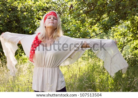 Pretty blonde woman feeling free in summer. Outdoor shot against a natural green background with a slight motion blur at the outstretched arms.
