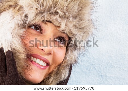 Beautiful woman in winter clothes with a bright smile. Studio shot against a light blue background as a wintry close up portrait with copy space