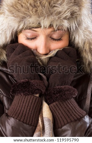 Beautiful young woman with closed eyes in winter clothes covers her face to protect from the cold. Studio shot as a wintry close up portrait
