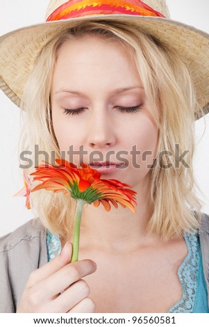 Portrait of a young blonde woman with closed eyes smelling at a red gerbera.
