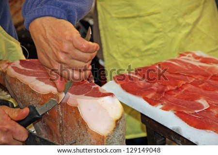 hand of butcher and knife during preparation of raw ham