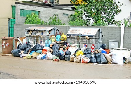 bags of rubbish and waste bins in the middle of the road full of mud