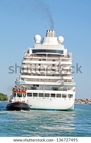 giant cruise ship for the transportation of passengers pulled by a tugboat out of the marina
