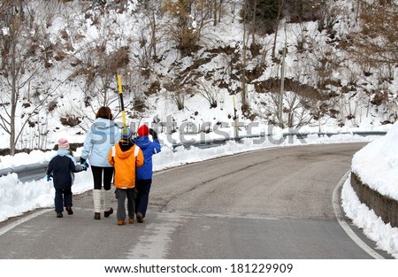 young family with three children walking on snow-covered road in the mountains in winter