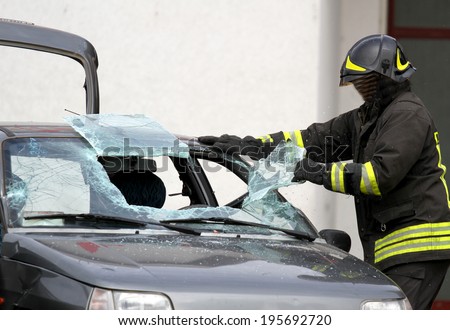 Fireman with protective overalls and work gloves while breaking a car windshield to release the people injured after car accident
