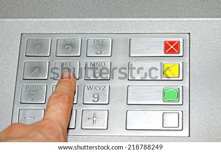 hand typing the secret code in the keyboard of an ATM to withdraw cash
