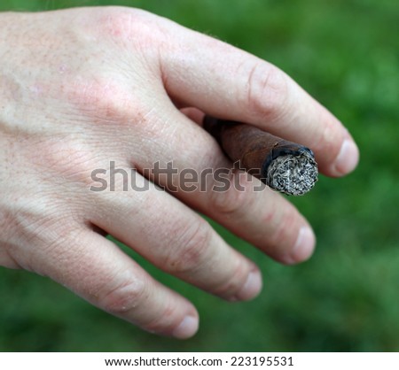Avid smoker\'s hand while holding the cigar between his fingers
