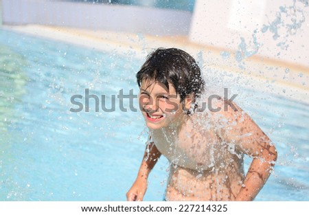 boy under the powerful jet of water in the pool in summer