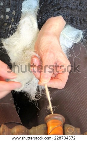 elderly woman works the wool with an old spinning wheel