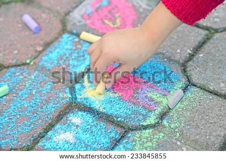young girl draws with the colourful chalks on the road