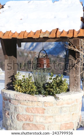 ancient well with bucket and snow on the roof in mountain village