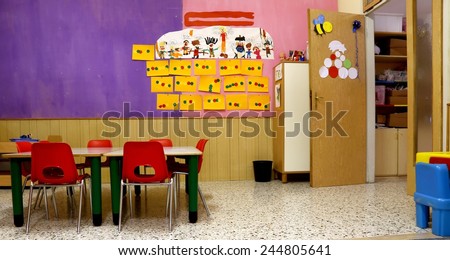 Preschool classroom with red chairs and table with drawings of children hanging on the walls
