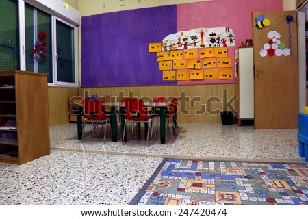 Preschool classroom with red chairs and table with drawings of children hanging on the walls