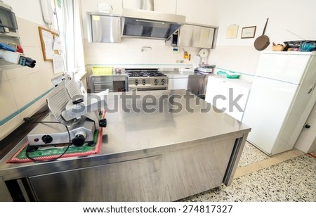 huge stainless steel kitchen with gas stove and an industrial meat slicer
