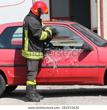 chief fireman whit red helmet while breaking the glass of a car with a special equipment