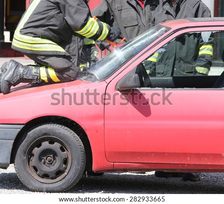 fireman with red helmet cuts the windshield  of car with a special saw