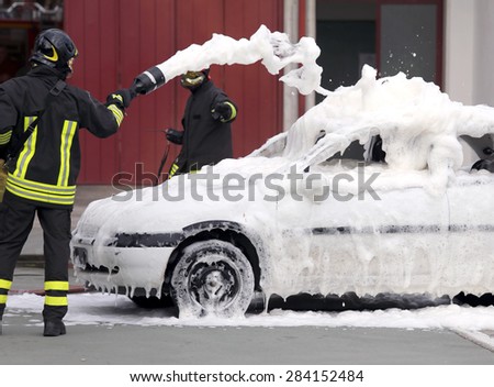 firemen during exercise to extinguish a fire in a car with foam