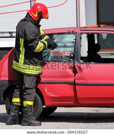 chief fireman whit red helmet while breaking the glass of a car with a special equipment