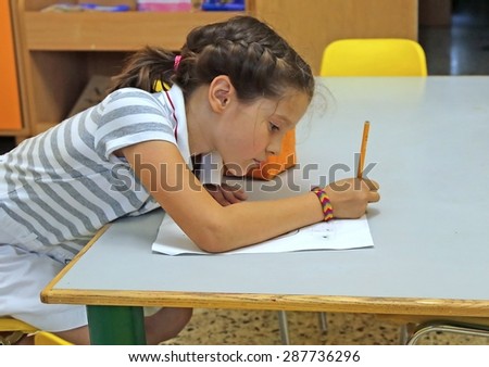 child writes on paper with pencil in classroom at school