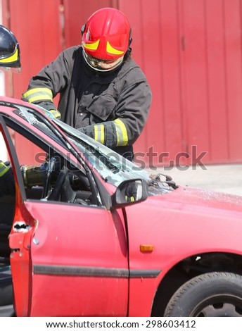 chief fireman whit red helmet while breaking the windshield of a car after traffic accident