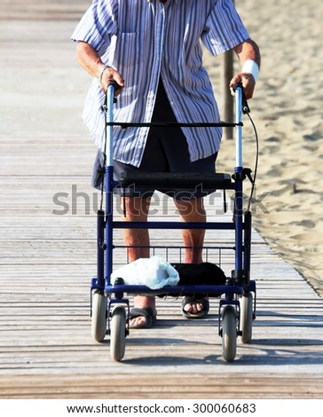 old man walking with Walker on the beach in summer