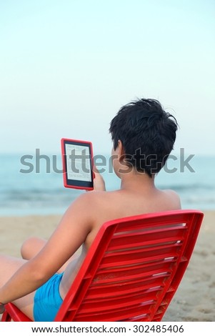 young boy reads the ebook on the sea shore in summer