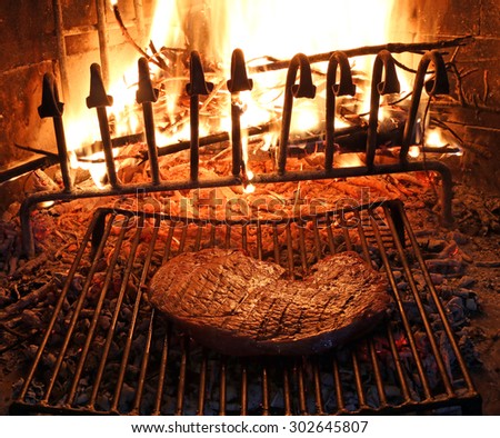 huge beef steak cooked on the barbeque fireplace with flame