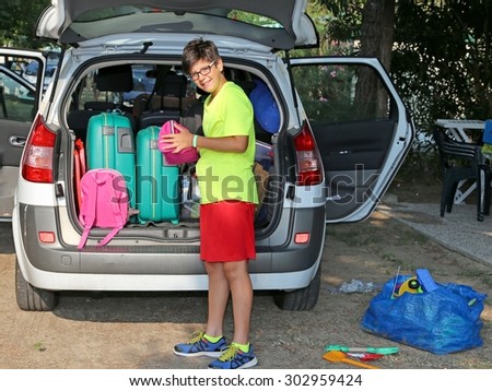 smiling boy loads bags in the baggage car in summer before departure