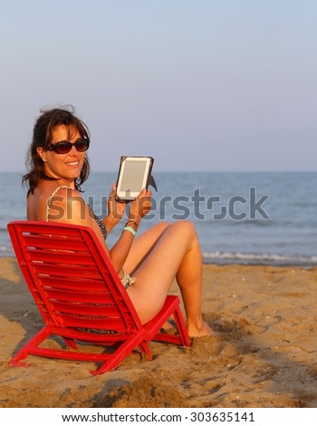 beautiful woman in swimsuit reads the ebook on the beach by the sea in summer